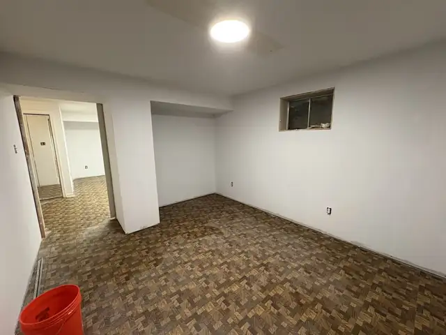 Basement room with finished, primed white drywall, a ceiling light and two small windows